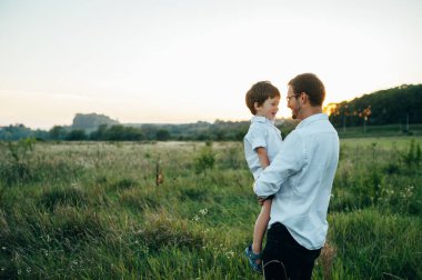Yakışıklı baba ve küçük tatlı oğlu yeşil çimenlikte eğleniyor ve oynuyorlar. Mutlu aile kavramı. Aile hayatı olan güzel doğa manzarası. Aile birlikte dinleniyor. Babalar Günü