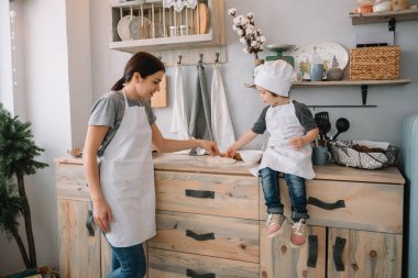 Genç mutlu anne ve bebeği mutfakta kurabiye pişiriyor. Noel ev yapımı zencefilli çörek. Beyaz üniformalı, şapkalı, çikolatalı kurabiyeli tatlı çocuk.