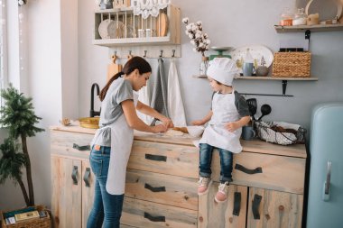 Genç mutlu anne ve bebeği mutfakta kurabiye pişiriyor. Noel ev yapımı zencefilli çörek. Beyaz üniformalı, şapkalı, çikolatalı kurabiyeli tatlı çocuk.