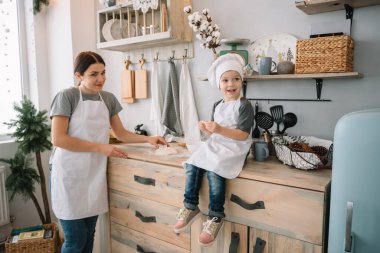 Genç mutlu anne ve bebeği mutfakta kurabiye pişiriyor. Noel ev yapımı zencefilli çörek. Beyaz üniformalı, şapkalı, çikolatalı kurabiyeli tatlı çocuk.