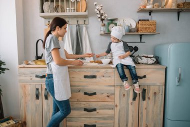Genç mutlu anne ve bebeği mutfakta kurabiye pişiriyor. Noel ev yapımı zencefilli çörek. Beyaz üniformalı, şapkalı, çikolatalı kurabiyeli tatlı çocuk.