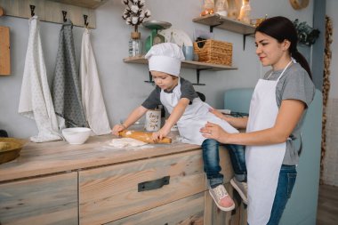 Genç mutlu anne ve bebeği mutfakta kurabiye pişiriyor. Noel ev yapımı zencefilli çörek. Beyaz üniformalı, şapkalı, çikolatalı kurabiyeli tatlı çocuk.