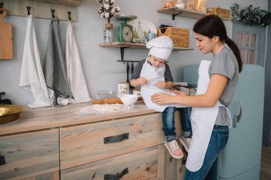 Genç mutlu anne ve bebeği mutfakta kurabiye pişiriyor. Noel ev yapımı zencefilli çörek. Beyaz üniformalı, şapkalı, çikolatalı kurabiyeli tatlı çocuk.