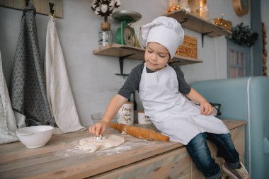 Genç mutlu anne ve bebeği mutfakta kurabiye pişiriyor. Noel ev yapımı zencefilli çörek. Beyaz üniformalı, şapkalı, çikolatalı kurabiyeli tatlı çocuk.