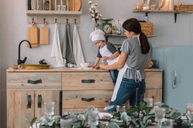 Genç mutlu anne ve bebeği mutfakta kurabiye pişiriyor. Noel ev yapımı zencefilli çörek. Beyaz üniformalı, şapkalı, çikolatalı kurabiyeli tatlı çocuk.