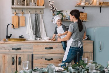 Genç mutlu anne ve bebeği mutfakta kurabiye pişiriyor. Noel ev yapımı zencefilli çörek. Beyaz üniformalı, şapkalı, çikolatalı kurabiyeli tatlı çocuk.