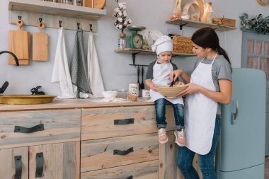Genç mutlu anne ve bebeği mutfakta kurabiye pişiriyor. Noel ev yapımı zencefilli çörek. Beyaz üniformalı, şapkalı, çikolatalı kurabiyeli tatlı çocuk.