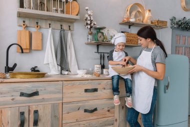 Genç mutlu anne ve bebeği mutfakta kurabiye pişiriyor. Noel ev yapımı zencefilli çörek. Beyaz üniformalı, şapkalı, çikolatalı kurabiyeli tatlı çocuk.