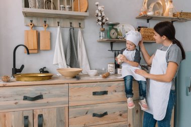 Genç mutlu anne ve bebeği mutfakta kurabiye pişiriyor. Noel ev yapımı zencefilli çörek. Beyaz üniformalı, şapkalı, çikolatalı kurabiyeli tatlı çocuk.