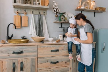 Genç mutlu anne ve bebeği mutfakta kurabiye pişiriyor. Noel ev yapımı zencefilli çörek. Beyaz üniformalı, şapkalı, çikolatalı kurabiyeli tatlı çocuk.
