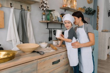 Genç mutlu anne ve bebeği mutfakta kurabiye pişiriyor. Noel ev yapımı zencefilli çörek. Beyaz üniformalı, şapkalı, çikolatalı kurabiyeli tatlı çocuk.