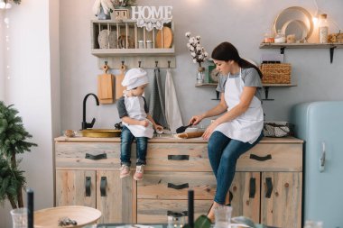 Genç mutlu anne ve bebeği mutfakta kurabiye pişiriyor. Noel ev yapımı zencefilli çörek. Beyaz üniformalı, şapkalı, çikolatalı kurabiyeli tatlı çocuk.