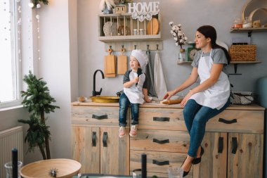 Genç mutlu anne ve bebeği mutfakta kurabiye pişiriyor. Noel ev yapımı zencefilli çörek. Beyaz üniformalı, şapkalı, çikolatalı kurabiyeli tatlı çocuk.