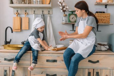 Genç mutlu anne ve bebeği mutfakta kurabiye pişiriyor. Noel ev yapımı zencefilli çörek. Beyaz üniformalı, şapkalı, çikolatalı kurabiyeli tatlı çocuk.