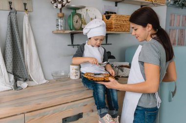 Genç mutlu anne ve bebeği mutfakta kurabiye pişiriyor. Noel ev yapımı zencefilli çörek. Beyaz üniformalı, şapkalı, çikolatalı kurabiyeli tatlı çocuk.