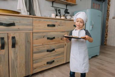 Genç mutlu anne ve bebeği mutfakta kurabiye pişiriyor. Noel ev yapımı zencefilli çörek. Beyaz üniformalı, şapkalı, çikolatalı kurabiyeli tatlı çocuk.