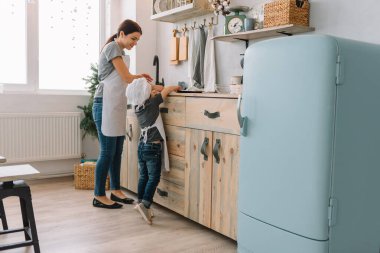 Genç mutlu anne ve bebeği mutfakta kurabiye pişiriyor. Noel ev yapımı zencefilli çörek. Beyaz üniformalı, şapkalı, çikolatalı kurabiyeli tatlı çocuk.