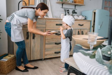 Genç mutlu anne ve bebeği mutfakta kurabiye pişiriyor. Noel ev yapımı zencefilli çörek. Beyaz üniformalı, şapkalı, çikolatalı kurabiyeli tatlı çocuk.