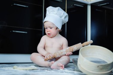 Küçük çocuk mutfakta halıda oturup tencerelerle oynuyor. Evde mutfakta yemek pişiren tatlı çocuk..