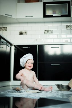 Küçük çocuk mutfakta halıda oturup tencerelerle oynuyor. Evde mutfakta yemek pişiren tatlı çocuk..