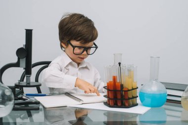 Mikroskop ve beyaz arka planda çeşitli renkli mataraları olan çocuk. Laboratuvarda deney yapan bir çocuk. Laboratuvarda patlama oldu. Bilim ve eğitim.