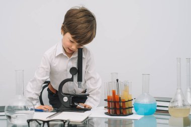 Mikroskop ve beyaz arka planda çeşitli renkli mataraları olan çocuk. Laboratuvarda deney yapan bir çocuk. Laboratuvarda patlama oldu. Bilim ve eğitim.