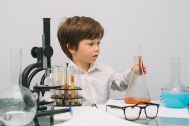 Mikroskop ve beyaz arka planda çeşitli renkli mataraları olan çocuk. Laboratuvarda deney yapan bir çocuk. Laboratuvarda patlama oldu. Bilim ve eğitim.