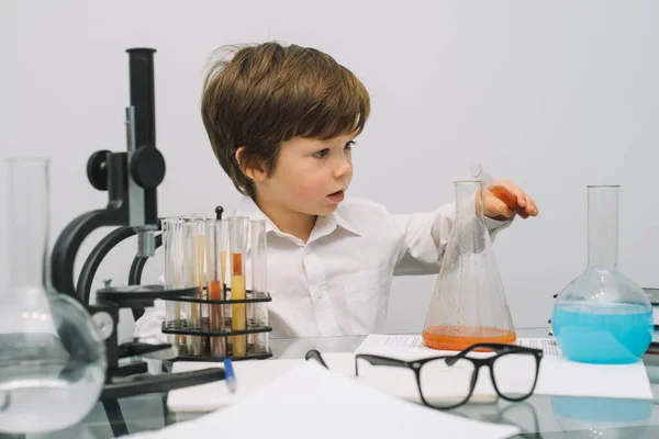 The boy with a microscope and various colorful flasks on a white background. A boy doing experiments in the laboratory. Explosion in the laboratory. Science and education.