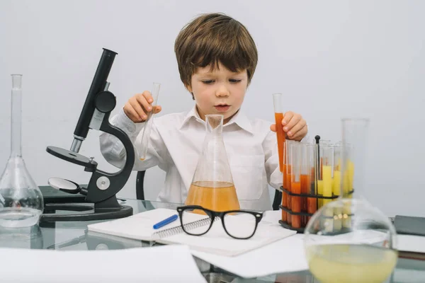 Chłopiec Mikroskopem Różnymi Kolorowymi Kolbami Białym Tle Chłopiec Przeprowadzający Eksperymenty — Zdjęcie stockowe
