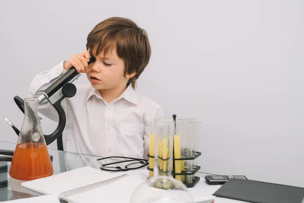 The boy with a microscope and various colorful flasks on a white background. A boy doing experiments in the laboratory. Explosion in the laboratory. Science and education.