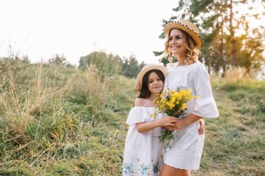 Neşeli anne ve küçük kızı yaz arkaplanında birlikte eğleniyorlar. Doğada yaşayan mutlu bir aile. Renkli çiçekli şirin kızlar..