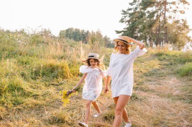 Neşeli anne ve küçük kızı yaz arkaplanında birlikte eğleniyorlar. Doğada yaşayan mutlu bir aile. Renkli çiçekli şirin kızlar..