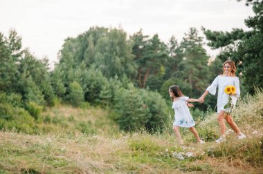 Neşeli anne ve küçük kızı yaz arkaplanında birlikte eğleniyorlar. Doğada yaşayan mutlu bir aile. Renkli çiçekli şirin kızlar..