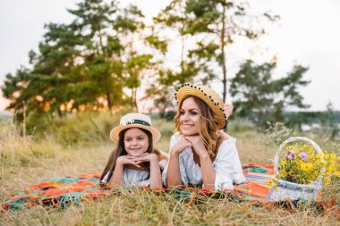 Mutlu bir kadın gülümsüyor ve küçük sevimli çocuğuyla oynuyor, dışarıda yatıyor. Sevgi dolu bir anne ve kız parkta birlikte vakit geçiriyorlar. Anne ve çocuk eğleniyor. Anneler Günü.