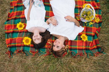 Mutlu bir kadının gülümsemesi ve küçük sevimli çocuğuyla oynaması, açık havada yatması. Sevgi dolu anne ve kızı parkta birlikte vakit geçiriyorlar. Anne ve çocuk eğleniyor. Anneler Günü.