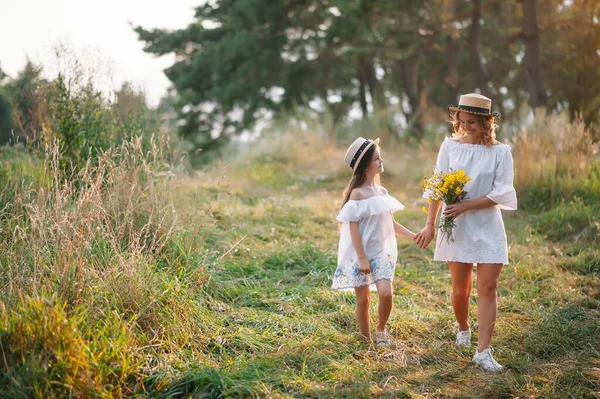 陽気な母親と彼女の小さな娘は夏の背景で一緒に楽しんでいます 自然の中で幸せな家族 可憐な花を持つかわいい女の子 — ストック写真