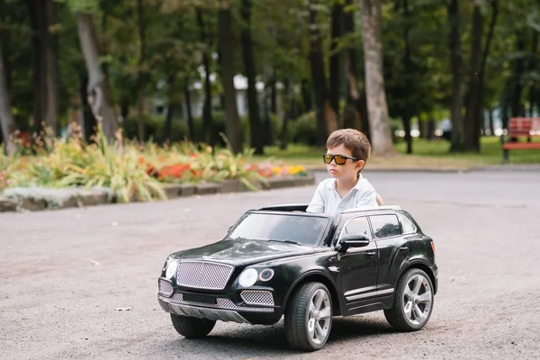 Parkta siyah elektrikli araba süren sevimli çocuk. Komik çocuk elektrikli bir oyuncak arabaya biniyor. Parkta siyah elektrikli araba süren küçük mutlu çocuk. Boşluğu kopyala.
