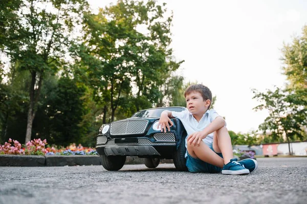 公園で黒い電気自動車に乗ってかわいい少年 面白い少年はおもちゃの電気自動車に乗っています 公園で黒い電気自動車に乗ってる幸せな少年 スペースのコピー — ストック写真