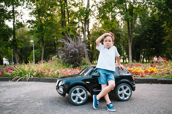 公園で黒い電気自動車に乗ってかわいい少年 面白い少年はおもちゃの電気自動車に乗っています 公園で黒い電気自動車に乗ってる幸せな少年 スペースのコピー — ストック写真