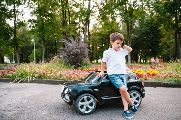 公園で黒い電気自動車に乗ってかわいい少年 面白い少年はおもちゃの電気自動車に乗っています 公園で黒い電気自動車に乗ってる幸せな少年 スペースのコピー — ストック写真