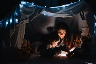 Mutlu bir aile babası ve çocuğu evdeki çadırda el feneriyle kitap okuyor. aile kavramı