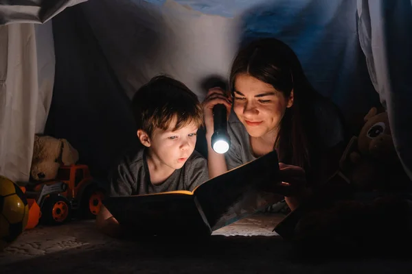 Mutlu bir aile babası ve çocuğu evdeki çadırda el feneriyle kitap okuyor. aile kavramı