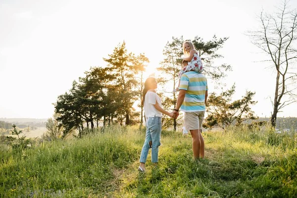 公園を歩く幸せな家族 母親と父親と娘は屋外で歩き 両親は赤ん坊の女の子の手を握っている 子供時代 家族の絆 結婚の概念 — ストック写真