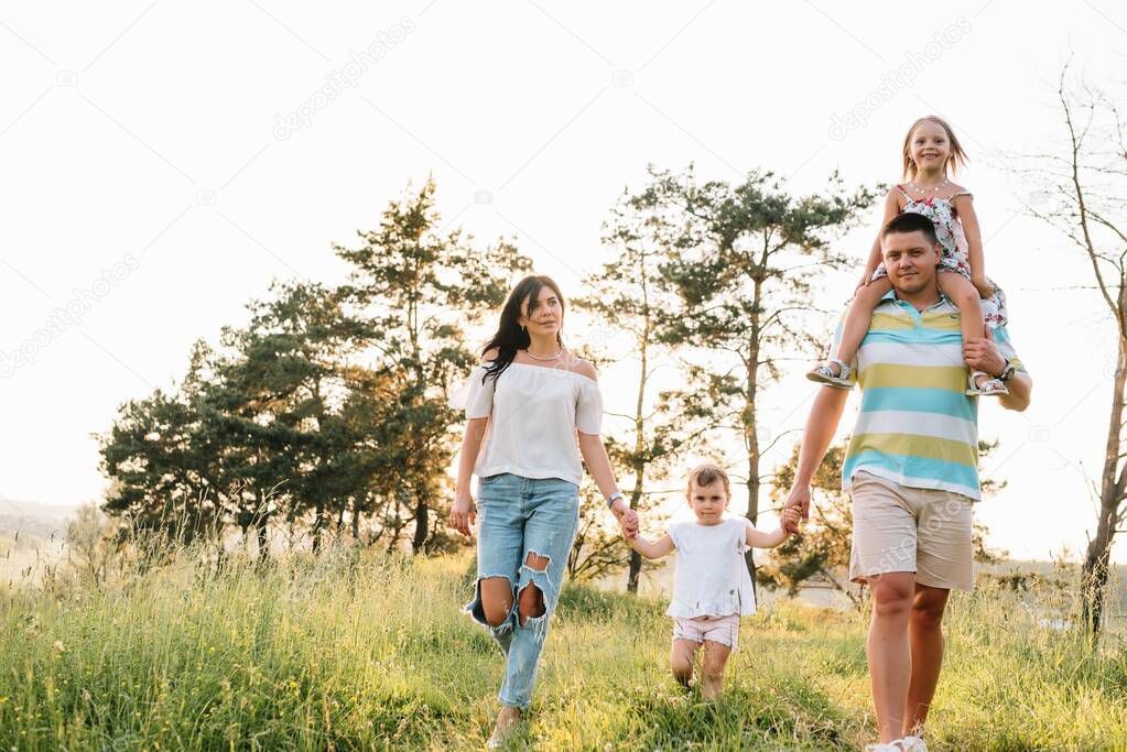 Happy family walking in the park. Mom, dad and daughter walk outdoors, parents holding the baby girl's hands. Childhood, parenthood, family bonds, marriage concept