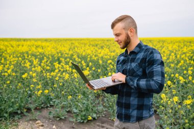 Genç tarımcı tecavüz alanında dizüstü bilgisayar tutuyor. Tarım sektörü konsepti. Yaz aylarında tecavüz alanında dizüstü bilgisayarla duran tarım mühendisi.