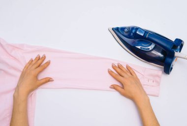 Kadın el ütüleme giysileri beyaz arka planda izole üst görünüm. Demiri ütüleyen adamın gömleğini giyen genç bir kadın ev işi sırasında yukarıdan görülmüş. Mavi ütü beyaz masada..