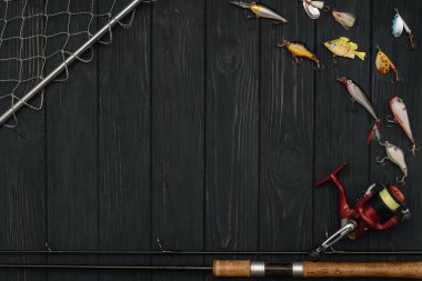 Fishing tackle - fishing spinning, hooks and lures on darken wooden background. Top view.