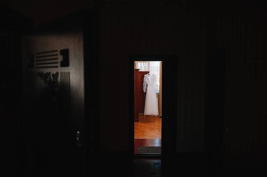 Güzel gelinin beyaz gelinliği, altında çiçekler olan bir otel odasında yatağın yanında asılı duruyor. Törenden önce gelin sabahı.