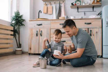 Mutfakta fırın çarşafı olan genç bir adam ve oğlu. Baba ve küçük oğlu mutfakta.
