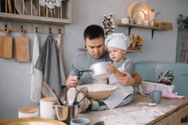 Mutfakta fırın çarşafı olan genç bir adam ve oğlu. Baba ve küçük oğlu mutfakta. Evde kal..